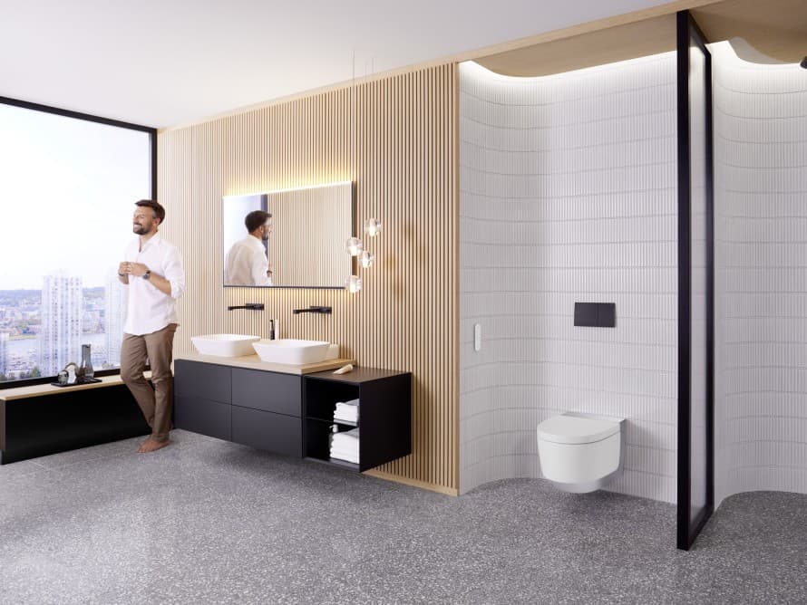 Man in large bathroom with dark furniture and Geberit AquaClean shower toilet